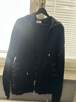 Svart pufferjacka från Moncler - Snygg svart pufferjacka från Moncler med quiltade partier och huva. Jackan har dragkedja framtill, två fickor och Moncler-logga på ärmen. Size XL, fungerar även på L.