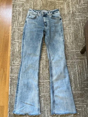 Ljusblå bootcut jeans från Zara - Säljer ett par ljusblå bootcut jeans från Zara med råa, fransiga benslut och klassisk femficksmodell. Perfekta för dig som gillar retrostil och vill ha ett par unika jeans.