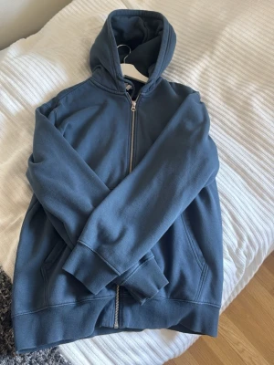 Blå zip-hoodie med huva - En stilren blå hoodie med dragkedja och huva. Tröjan har ribbade muddar vid ärmslut och nederkant samt två fickor framtill. Perfekt för en avslappnad look och gjord i mjukt sweatshirtmaterial. Storlek Small, MAN