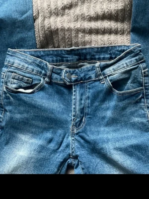 Blå bootcut jeans med slitningar - Säljer ett par blå bootcut jeans med lätt slitna detaljer och klassisk femficksdesign. Jeansen har normalhög midja och är tillverkade i denim med en snygg tvättad look. Perfekta för en avslappnad och trendig stil.