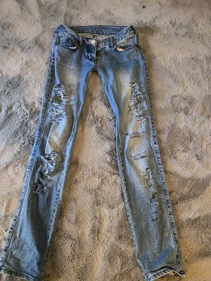 Ljusblå slitna bootcut - Snygga ljusblå bootcut jeans med kraftiga slitningar och trasiga detaljer längs båda benen. Jeansen har klassisk femficksdesign och låg midja. Perfekta för en avslappnad och trendig streetstil.