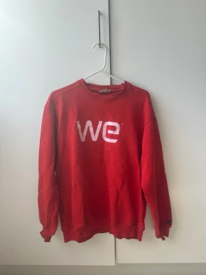Röd sweatshirt med WE-tryck - Cool röd sweatshirt med vitt WE-tryck på bröstet. Tröjan har rund halsringning och långa ärmar, perfekt för en avslappnad och trendig look. Materialet känns mjukt och bekvämt, och passformen är normal. Ett enkelt statement-plagg för garderoben.