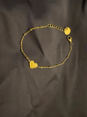 Guldigt armband med hjärta - Snyggt och enkelt armband i guldfärgad metall med en liten hjärtformad detalj i mitten. Kedjan är tunn och har justerbar längd med karbinlås. Ordinarie pris 350kr💕Passar perfekt för dig som gillar eleganta och simpla smycken!! Armbandet är i rostfritt stål!