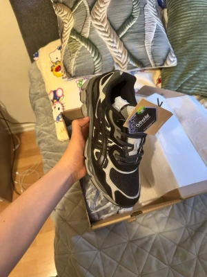 Asic gel nyc svart 42 storlek - Snygga Asics sneakers i svart och vitt med meshpaneler och detaljer i syntet. Skorna har klassisk snörning och en robust sula som ger bra grepp. Perfekta för dig som gillar sportig stil och vill ha bekväma skor till vardags. Ikonisk Asics-logga på sidan.