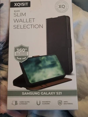 XQISIT Slim Wallet mobilskal S21 - Slim Wallet Selection mobilskal för Samsung Galaxy S21 i svart med kortfack och magnetisk stängning. Utsidan är svart och insidan brun, tillverkad i konstläder och plast. Ger 360° skydd och har antibakteriella egenskaper. Perfekt för dig som vill ha både skydd och plats för kort.