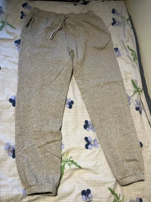 Gråa mjukisbyxor med dragsko - Säljer ett par klassiska gråa mjukisbyxor med resår i midjan och dragsko. Byxorna har även resår vid bensluten och sidofickor. Perfekta för chill dagar eller när du vill vara bekväm. Materialet känns mjukt och skönt mot huden.