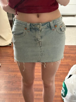 Ljusblå jeanskjol från True Religion - Säljer en ljusblå kort jeanskjol från True Religion med råa kanter och klassiska fickor fram och bak. Kjolen har snygga broderade detaljer på bakfickorna och knappstängning framtill. Perfekt för dig som gillar en avslappnad och trendig stil.