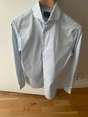 Ljusblå skjorta från Selected homme  - Klassisk ljusblå skjorta från selected homme med lång ärm och knappar framtill. Skjortan har en stilren design med normal passform och är tillverkad i mjuk bomull. Perfekt till både jeans och kostym. Slim fit