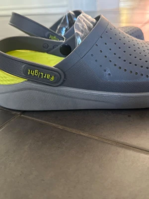 Grå tofflor från Fairlight - Snygga grå tofflor från Fairlight med ventilerande hål och justerbar hälrem. Insidan har en limegrön, strukturerad sula för extra komfort. Tillverkade i lätt och tålig plast, perfekta för chill dagar hemma eller på stranden.