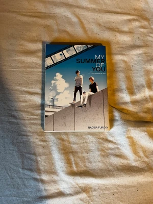 My Summer of You manga - Manga-bok med titeln 'My Summer of You' av Nagisa Furuya. Omslaget har en blå och vit färgskala med två killar på en betongmur och filmrulle i bakgrunden. Boken är på engelska och handlar om romantik mellan två killar och deras gemensamma filmintresse.