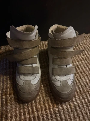 Vita och beige sneakers med kardborre - Sneakers i vitt och beige med  kardborreband och grönt parti vid hälen. Skorna har en hög modell och är tillverkade i en mix av läder och mocka. Klassisk liten upphöjd häl så väldigt bekväma att gå i.