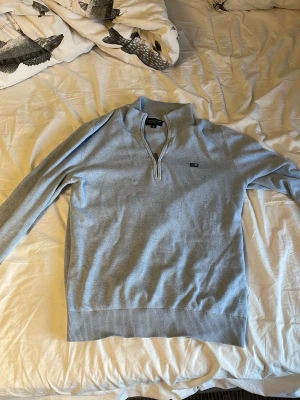 Ljusblå halvzip-tröja från lexington - Snygg ljusblå tröja från lexington med halv dragkedja och liten logga på bröstet. Tröjan har ribbade muddar och är tillverkad i ett mjukt, tunt material. Perfekt för lager-på-lager och stilrena outfits.