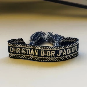Marinblått broderat armband  - Snyggt marinblått armband med text broderad i vitt. Armbandet är gjort i textil och har dekorativa tofsar i ändarna. Perfekt accessoar för att lyfta din stil.