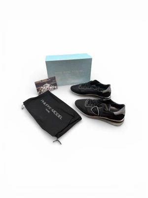 Philippe Model svarta sneakers - Svarta sneakers från Philippe Model med grå och vita detaljer. Skorna har en klassisk låg siluett, snörning och en vit/grå sula. Materialmix av mocka och textil ger en snygg och modern look. Perfekta för dig som gillar stilrena och trendiga sneakers.