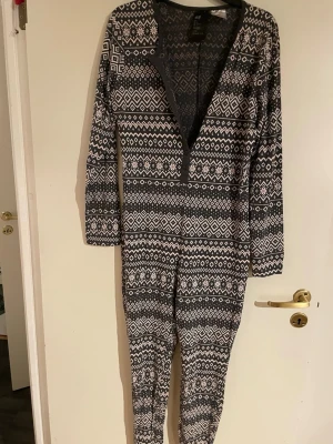 Mönstrad onesie med dragkedja - Mysig onesie med svartvitt nordiskt mönster och långa ärmar. Dragkedja framtill och åtsittande passform. Perfekt för chill hemma eller som loungewear. Mjuk och stretchig bomullsblandning som känns skön mot huden.