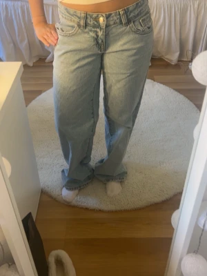 Ljusblå vida jeans från Gina tricot  - Säljer ett par ljusblå jeans från Gina tricot i vid modell med låg midja. Jeansen har klassiska fem fickor, gylf med dragkedja och knapp samt breda benslut för en avslappnad look. Perfekta till en casual outfit.