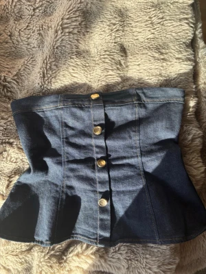 Mörkblå topp från Zara  - Trendig mörkblå topp från Zara med guldfärgade knappar framtill. Axelbandslös bandeau-modell som sitter tight och markerar midjan. Perfekt för att skapa en edgy look till både jeans och kjol.