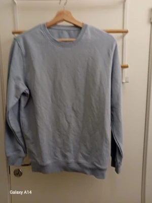Ljusblå sweatshirt med rund hals - En stilren ljusblå sweatshirt med rund halsringning och ribbade muddar vid ärmslut och nederkant. Tröjan har en relaxed passform och är tillverkad i mjukt material som känns skönt mot huden. Perfekt att matcha med jeans eller joggers.