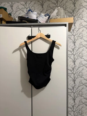 Svart linne/tröja - Snygg svart linne med breda axelband och rundad halsringning. Tight passform och ribbad struktur som ger en trendig look. Perfekt att styla med jeans eller kjol för en clean outfit.