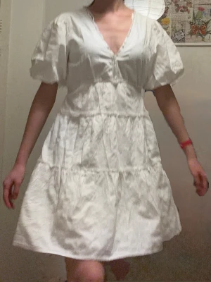 Vit klänning med  puffärm - HELT NY!!! Bara testad!!! Söt vit broderie anglaise klänning med blommigt mönster, v-ringning och puffiga korta ärmar. Klänningen har volangdetaljer och är sydd i ett lätt bomullstyg, perfekt för student eller skolavslutning. Den har en utsvängd passform och slutar ovanför knät. Snygg och stilren design. Nypris ~700