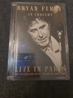 Bryan Ferry Live in Paris DVD - Konsert-DVD med Bryan Ferry, inspelad live i Paris på Le Grand Rex i mars 2000. Omslaget är svart med guldtext och har bilder från konserten. Innehåller låtar som 'Avalon', 'Jealous Guy' och 'Love Is The Drug'. Perfekt för fans av klassisk rock och liveframträdanden.