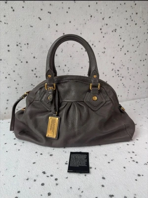 Mörkgrå Marc Jacobs läderväska - Säljer en mörkgrå vintage väska från Marc Jacobs i fint skick. En etikettlapp skickas med. Hör av dig vid några funderingar!