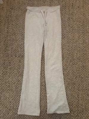 Ljusgrå mjukisbyxor med utsvängda ben Nelly  - Säljer ett par ljusgrå lågmidjade mjukisbyxor med utsvängda ben och dragsko i midjan. Byxorna är i mjukt och stretchigt material, perfekta för chill dagar. Passar dig som gillar en relaxed och trendig stil.