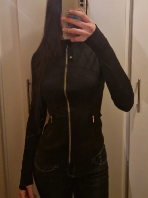 Svart slim vindjacka med dragkedja - Snygg svart vindjacka med figurnära passform och hel dragkedja framtill. Jackan har quiltade detaljer upptill, två fickor med dragkedja och hög krage. Perfekt för dig som vill ha en stilren och sportig look.