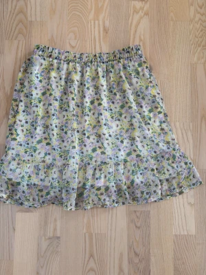 Blommig volangkjol från Vero Moda - Söt blommig kjol från Vero Moda med volangkant nedtill. Kjolen har elastisk midja och ett luftigt, lätt material i ljusa färger som vitt, gult, grönt och lila🫶🏻