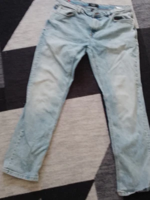 Ljusblå raka jeans - Säljer ett par ljusblå jeans med rak passform och klassisk femficksdesign. Jeansen har normal midja och dragkedja med knapp. Perfekta för en avslappnad och trendig stil.