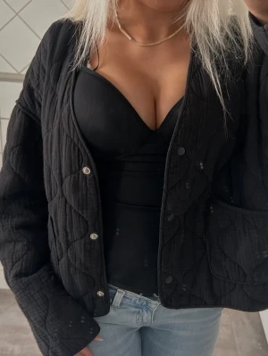 Svart quiltad cardigan med fickor - Säljer en svart quiltad cardiganjacka med tryckknappar och två framfickor. Jackan har en avslappnad passform och är tillverkad i ett mjukt, vadderat material som ger en cool och trendig look. Perfekt att slänga över en topp till jeans.