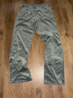 Gröna velour mjukisbyxor Juicy Couture - Snygga gröna mjukisbyxor i mjuk velour från Juicy Couture. Byxorna har dragsko i midjan och raka ben. Perfekta för en chill och avslappnad stil. Liten Juicy Couture-logga på fickan framtill.