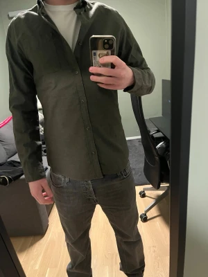 Mörkgrön skjorta  - Snygg mörkgrön skjorta från Jack & Jones Essentials i 100% bomull. Skjortan har klassisk krage, bröstficka och knappar framtill. Perfekt till lager på lager och enkel att styla med olika outfits.