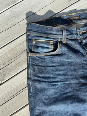 Mörkblå jeans från Nudie Jeans - Säljer ett par mörkblå selvage jeans ifrån Nudie Jeans. Ett par extremt snygga jeans med riktigt fina fades. Storlek W31 L32 och är i prima skick. Hör av dig vid fråga👍