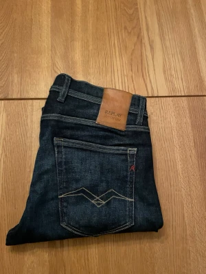 Mörkblå Replay jeans - Snygga mörkblå jeans från Replay med klassisk femficksmodell och kontrastsömmar. Jeansen har en skinnpatch med logga bak i midjan och diskret broderad detalj på bakfickan, Säljer jeansen då jag växt ur dom,  använda minimalt skicka ett meddelande så löser vi något!  Mvh 