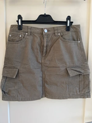 Grön cargokjol med fickor - Grön cargokjol med stora sidofickor och klassisk jeansknäppning fram. 