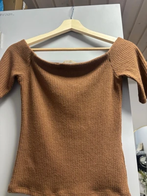 Brun ribbad offshoulder topp - Snygg brun ribbad topp med offshoulder-design och korta ärmar. Perfekt för dig som vill ha en enkel men trendig look. Materialet är mjukt och stretchigt, vilket gör den bekväm att bära hela dagen.