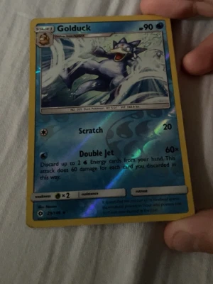 Pokémonkort Golduck holo - Säljer ett holografiskt Pokémonkort med Golduck-motiv. Kortet har blå och gula färger med en glansig yta och visar Golduck mitt i en vattenattack. Perfekt för samlare eller Pokémonfans som vill utöka sin kortsamling.