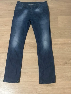 Mörkblå raka jeans  - Snygga mörkblå jeans med raka ben och diskreta slitningar på låren och bakfickorna. Klassisk femficksmodell med knapp och dragkedja. Jeansen har en modern tvättad look och passar perfekt till en avslappnad stil.