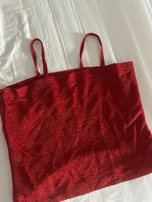 Glittrig röd linne - Säljer en glittrig röd linne  med två smala axelband. Tröjan är enkel och materialet skimrar snyggt i ljuset. Passar xs 