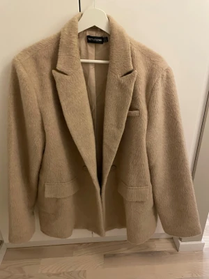 Beige lurvig kappa  - Stilren beige kappa från Petit Studio med lurvig textur och klassisk krage. Kappan har två framfickor.