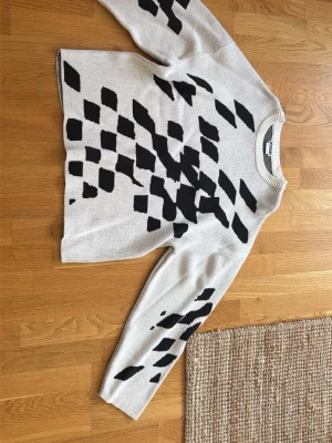 Stickad tröja med svart mönster Weekday - Säljer en beige stickad tröja från Weekday med svart grafiskt mönster över hela tröjan. Tröjan har rund halsringning och ribbade muddar vid hals, ärmslut och nederkant. Perfekt för dig som gillar en unik och trendig look.