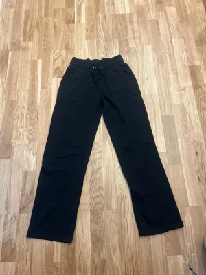 Svarta mjukisbyxor med raka ben - Säljer ett par svarta mjukisbyxor med raka ben och resår i midjan samt dragsko. Byxorna har två stora fickor fram och två bak. Perfekta för chill dagar eller när du vill vara bekväm. Materialet känns mjukt och skönt mot huden.