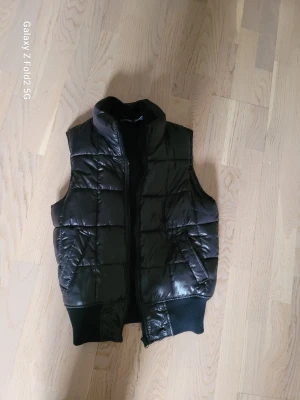 Svart dunväst från La Redoute - Snygg svart dunväst från La Redoute med quiltat mönster och hög krage. Västen har ribbade muddar nedtill och är fodrad med mjukt tyg på insidan. Perfekt för lager-på-lager och enkel att matcha med olika outfits.