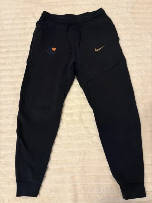 Mörkblå Nike x FC Barcelona mjukisbyxor - Mörkblå mjukisbyxor från Nike i samarbete med FC Barcelona. Byxorna har dragsko i midjan, ribbade muddar vid benslut och klubbens emblem samt Nike-logga framtill. Skön passform och sportig look, perfekta för chill eller träning.