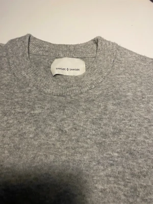 Grå stickad tröja från Samsøe Samsøe - Mysig ljusgrå stickad tröja från Samsøe Samsøe med rund halsringning och ribbade muddar. Det är en ull/alpacka/syntet blandning. Tröjan har en enkel och stilren design som passar perfekt till jeans. Materialet känns mjukt och behagligt mot huden. Passar som en regular fit. 