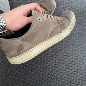 Bruna sneakers från Lanvin - Snygga bruna sneakers från Lanvin med snörning och en stilren design. Skorna har en vit sula och är tillverkade i mocka, vilket ger dem en lyxig känsla. Perfekta för en avslappnad men stilfull look. Skick 5/10 finns defekter. 