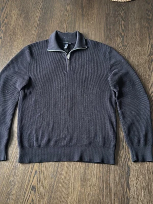 Mörkblå stickad halvziptröja - Snygg mörkblå stickad tröja med halv dragkedja och ståkrage. Tröjan har ribbade muddar vid ärmslut och nederkant, vilket ger en schysst passform. Perfekt för lager på lager och enkel att matcha med jeans eller chinos.