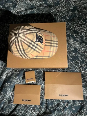 Burberry keps - Säljer en klassisk Burberry keps i beige med det klassiska rutmönstret och stor broderad B logga framtill. Storlek M,fint skick och perfekt att bära som huvudbonad nu när sommaren närmar sig. Säljer denna kepsen eftersom att den är för liten för mig nu, kvitto för kepsen finns.