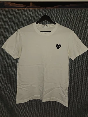 Vit t-shirt från Comme des Garçons Play - Vit t-shirt från Comme des Garçons Play med det ikoniska svarta hjärtat med ögon broderat på bröstet. Klassisk rund halsringning och korta ärmar. Tillverkad i mjuk bomull för en skön känsla. Sitter mer som S. Är öppen för prisförslag vid snabb försäljning.